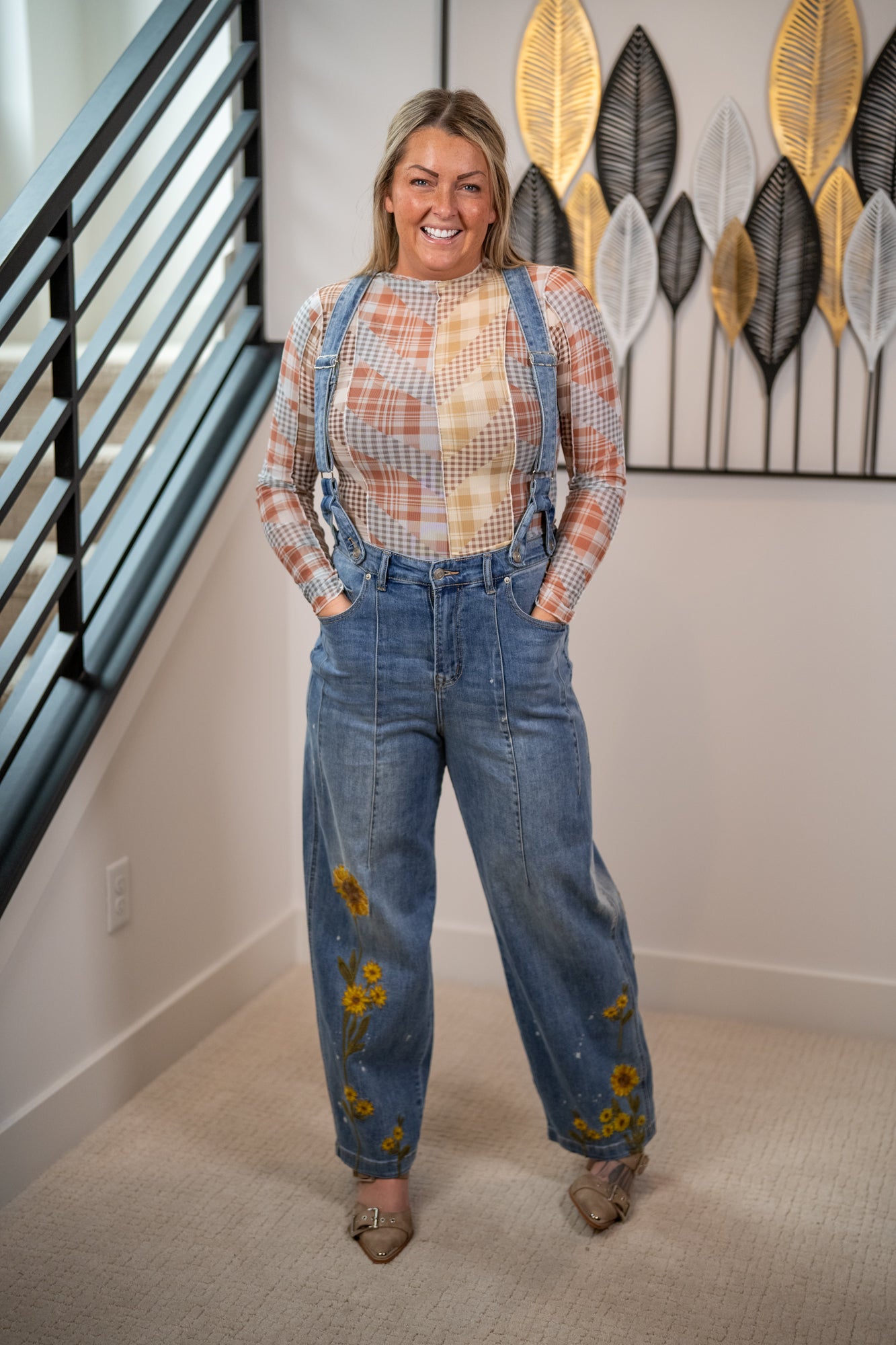 Woman wearing a plaid shirt and blue jeans with sunflower designs indoors.