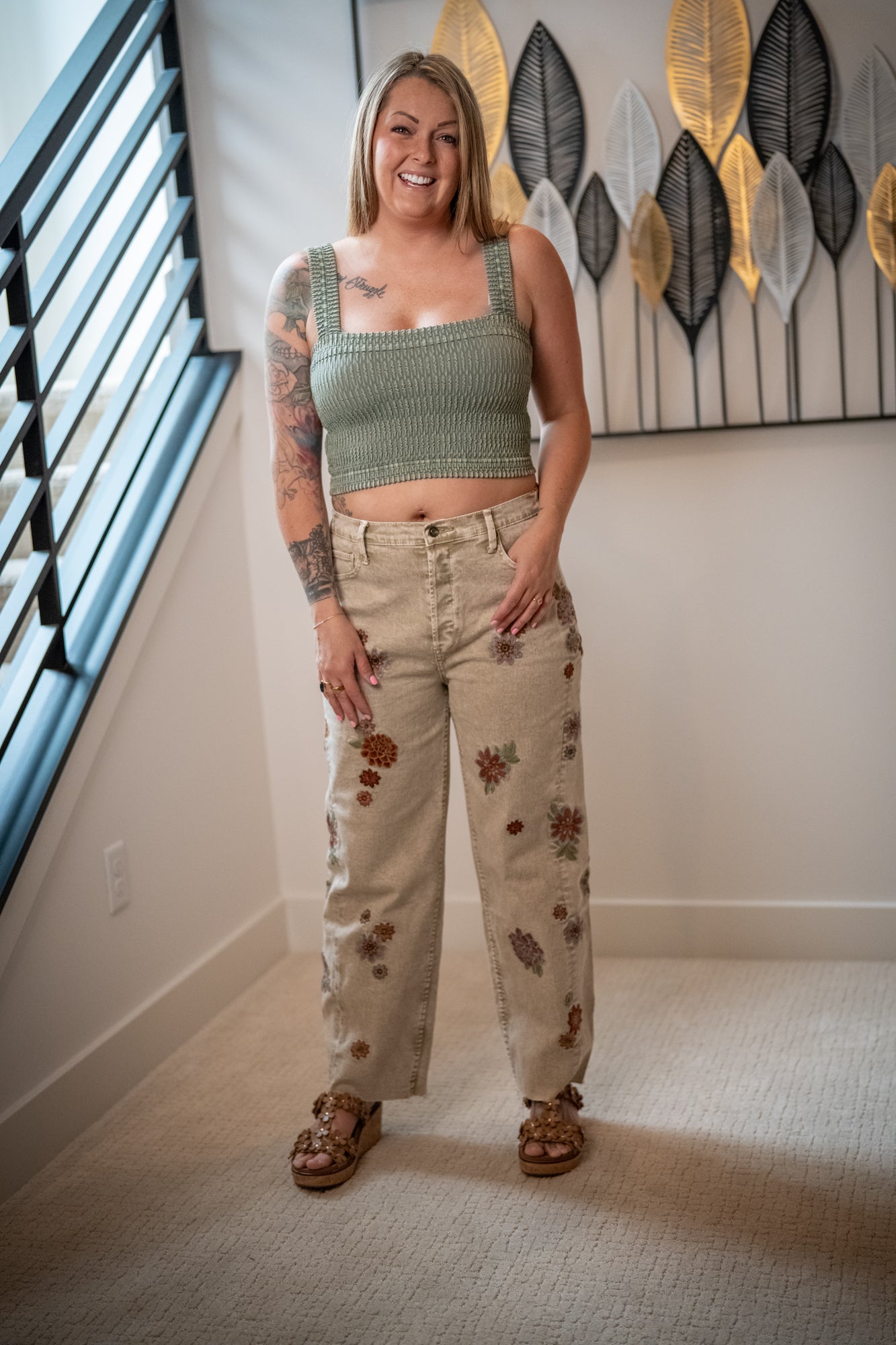 Woman wearing a green crop top and floral pants standing in a room with decorative wall art.