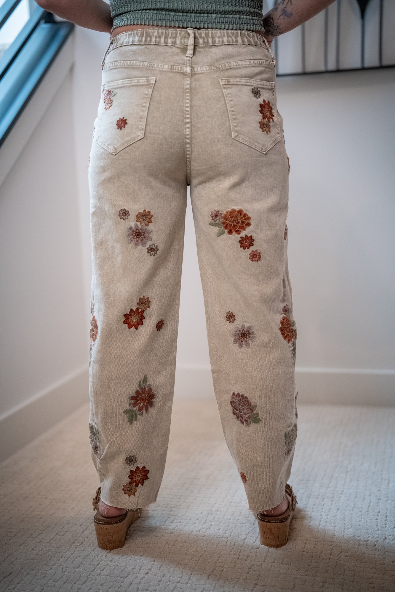 Light-colored jeans with floral patterns worn by a person indoors.