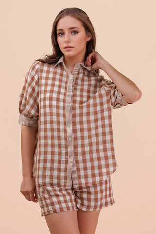 Woman wearing a brown and white checkered shirt and shorts set on a beige background
