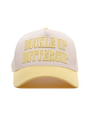 A structured baseball cap with a cream-colored front panel and brim, featuring gold embroidered text that reads 'BUCKLE UP BUTTERCUP' on the front. The cap is photographed against a seamless white background.