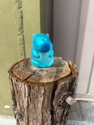 Blue plastic bear toy attached to a wooden log against a white wall.