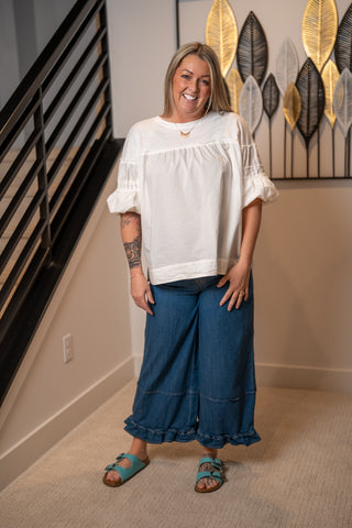 Woman wearing a white blouse and blue pants standing in a room with decorative wall art.