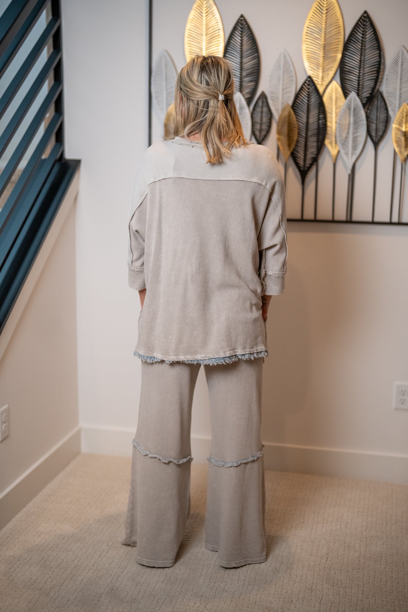 Person wearing a light gray outfit standing in a room with decorative wall art.