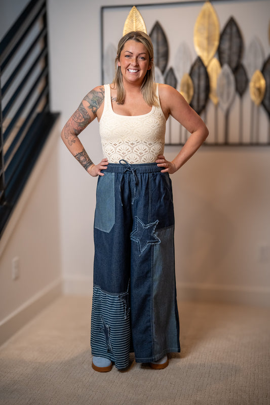 Woman wearing a white top and blue patchwork pants in a room with decorative wall art.