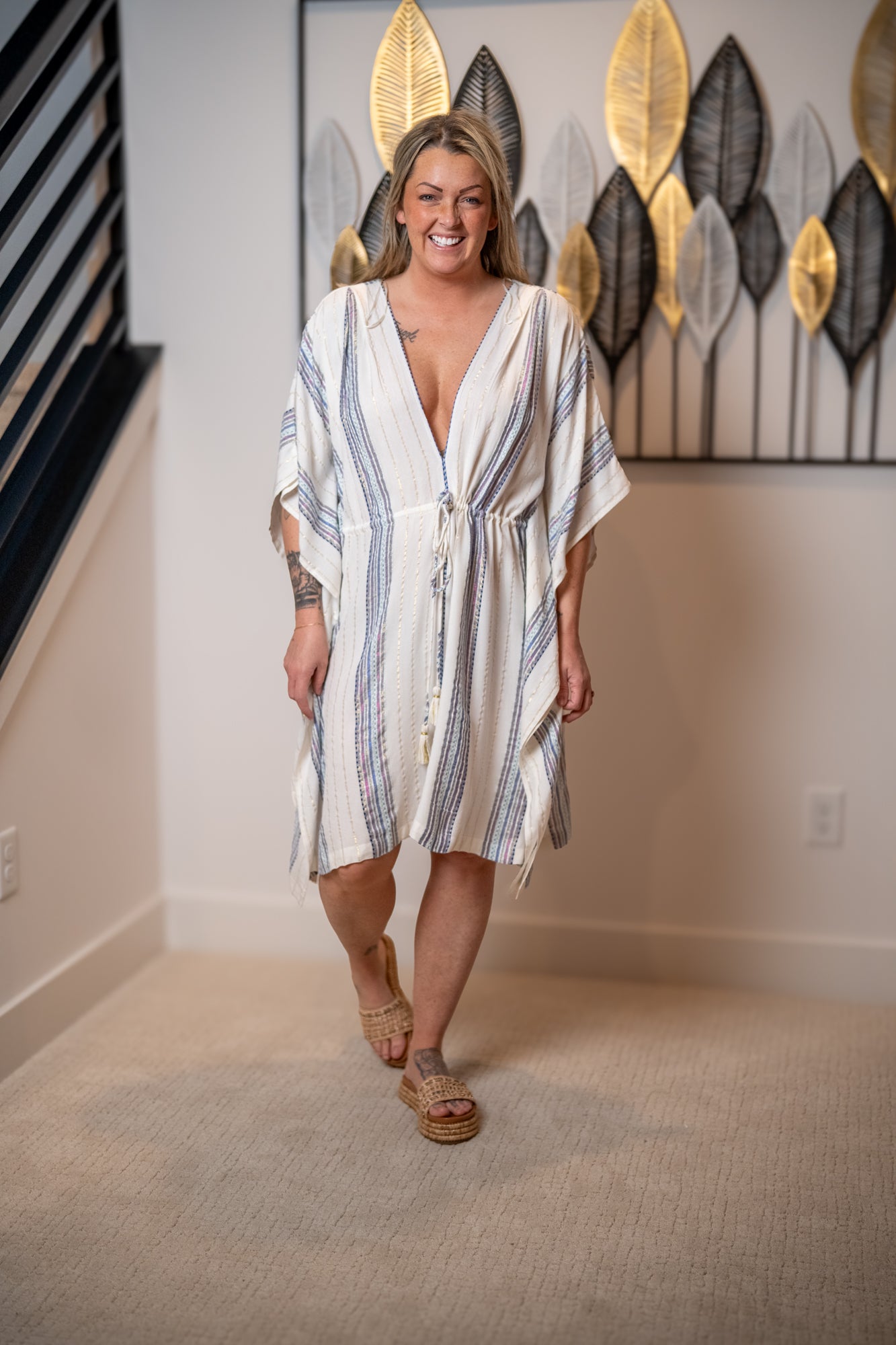 Woman wearing a white and blue striped dress in a room with decorative wall art.