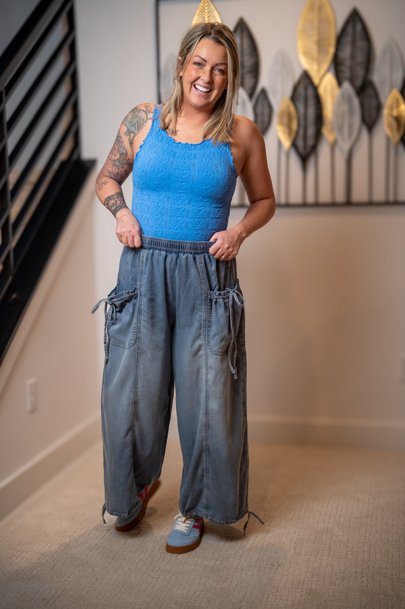 Woman wearing a blue tank top and wide-leg jeans standing in a room with decorative wall art.