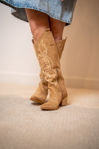 Tan cowboy boots with intricate designs worn by a person on a neutral background