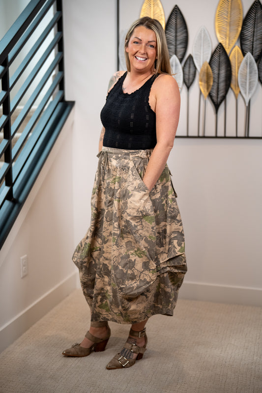 Woman wearing a black tank top and camouflage midi skirt with hands in pockets