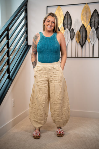 Woman wearing a blue top and beige pants standing in a room with decorative wall art.