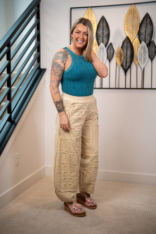 Woman wearing a blue top and beige pants standing in a room with decorative wall art.