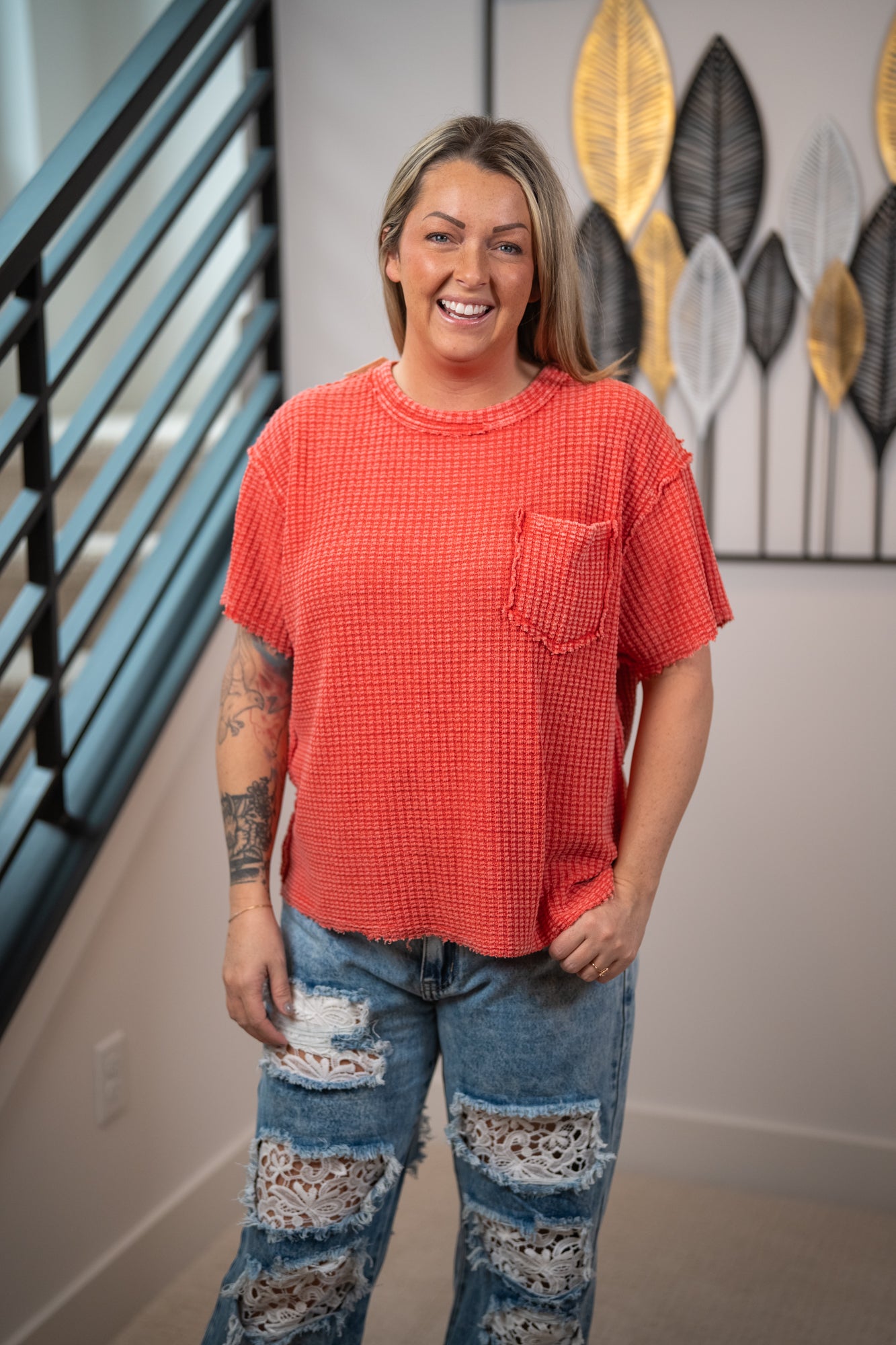 Person wearing a red checkered shirt and distressed jeans standing in a room with decorative wall art.