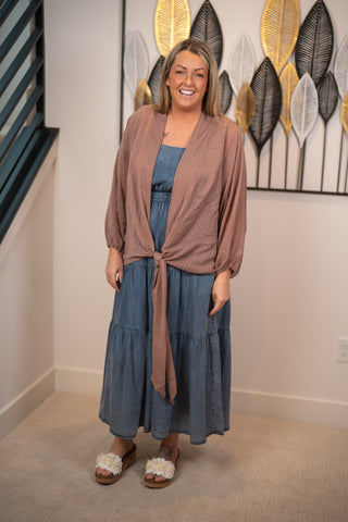 Woman wearing a blue dress and brown cardigan standing in a room with decorative wall art.