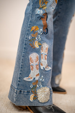 Close-up of embroidered jeans with cowboy boots and flowers on a blurred background