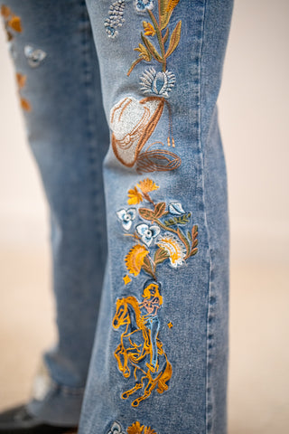Close up of Blue B western embroidered flare jeans with floral stitching, cowboy and boot design