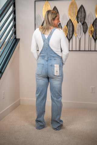 Back view of Risen light wash wide leg denim overalls with cross back straps and relaxed fit