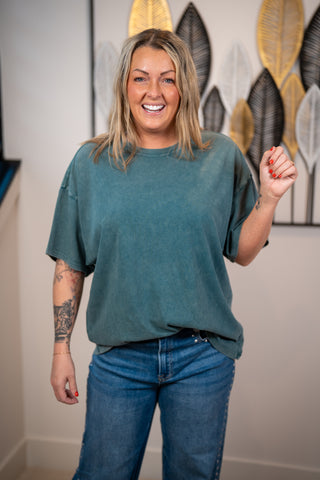 Person wearing a dark teal oversized shirt and jeans standing 