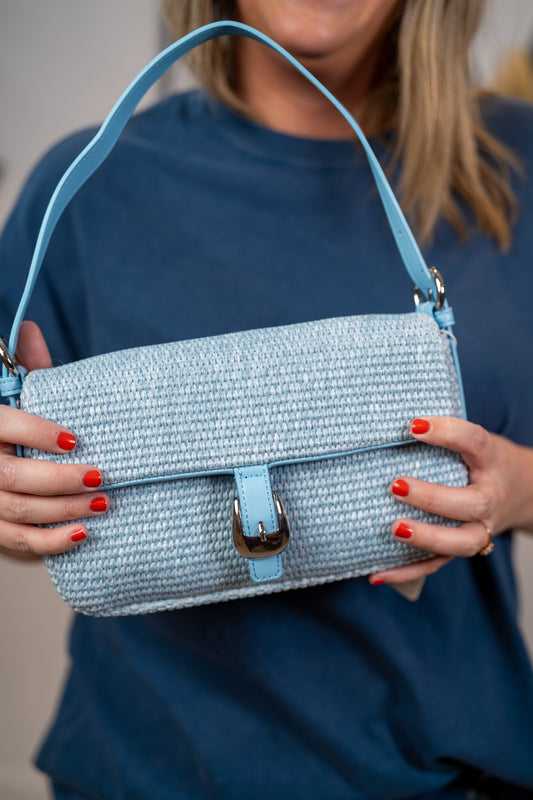 Close up of Light blue woven straw shoulder bag with silver hardware and adjustable strap