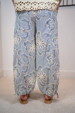Blue striped pants with white floral embroidery worn by a person on a light background