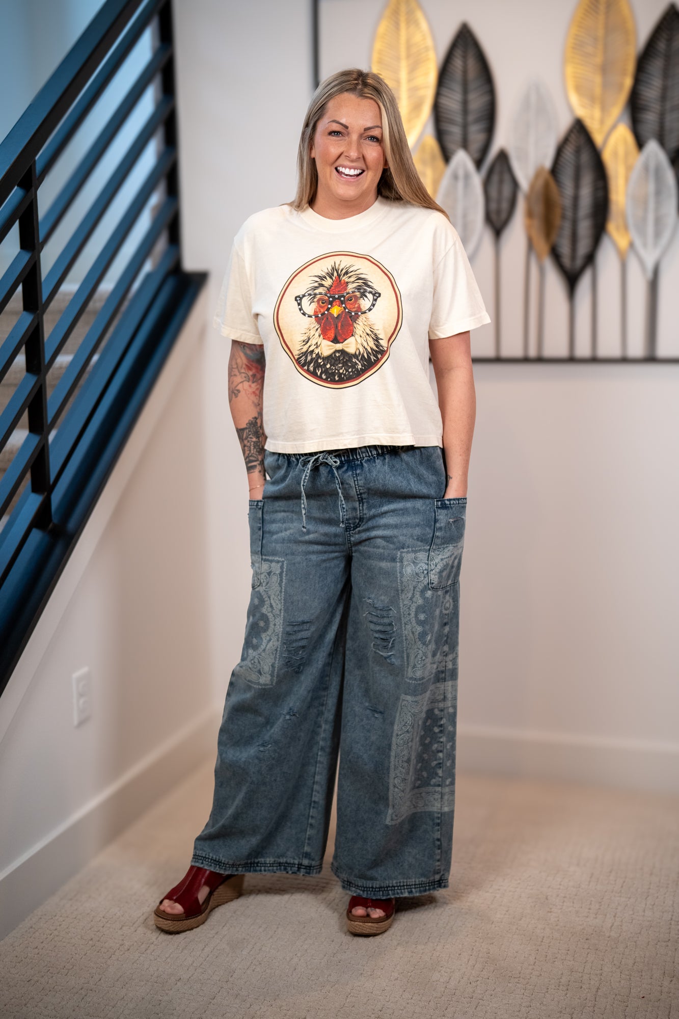 Woman wearing a graphic t-shirt and wide-leg jeans standing in a room with decorative wall art.