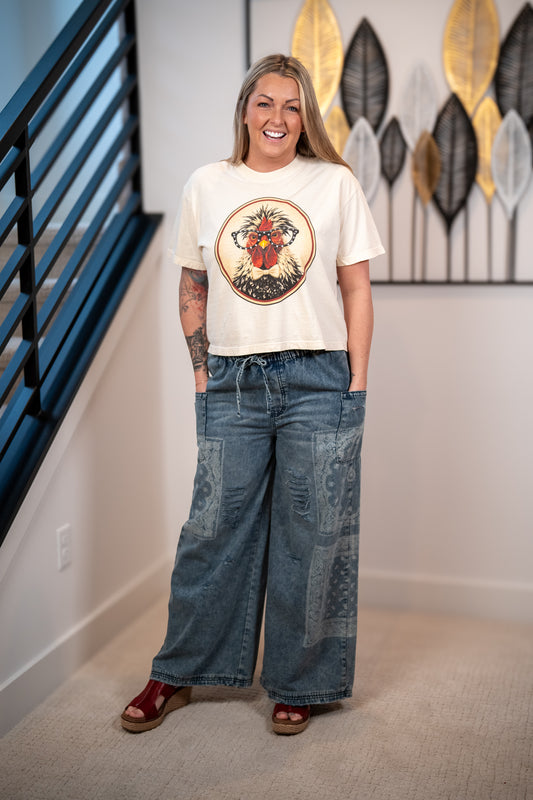 Woman wearing a graphic t-shirt and wide-leg jeans standing in a room with decorative wall art.