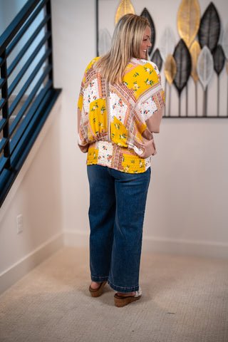 Woman wearing a colorful patterned blouse and blue jeans standing in a room with decorative wall art.