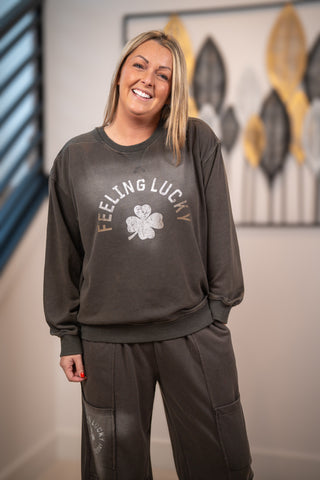 Person wearing a dark gray sweatshirt with 'Feeling Lucky' text and a clover graphic, standing indoors.