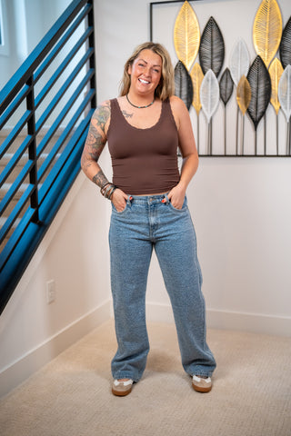 Woman wearing a brown tank top and rhinestone covered jeans standing