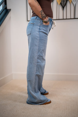Person wearing blue jeans and brown shoes standing on a carpeted floor.