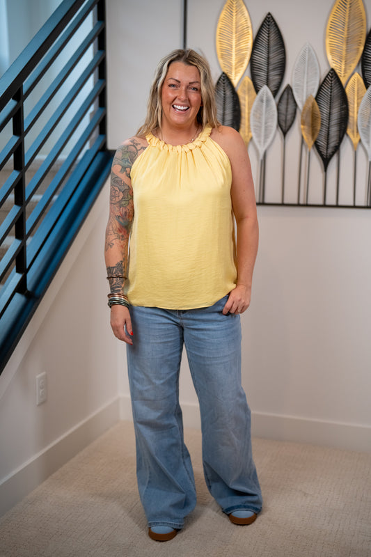 Woman wearing a yellow top and blue jeans standing in a room with decorative wall art.
