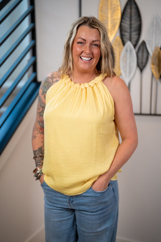 Woman wearing a yellow top and blue jeans standing in an indoor setting with decorative elements.