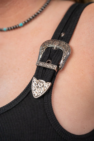 Black strap with decorative silver buckle on a person wearing a black top.