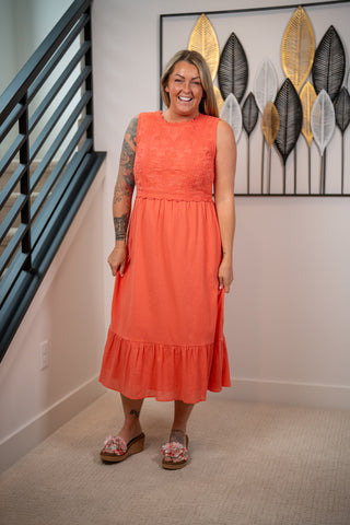 Woman in an orange dress standing in a room with decorative wall art.
