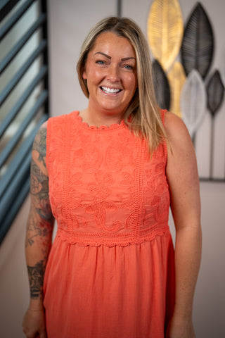 Woman wearing an orange dress with a decorative pattern, standing against a neutral background.
