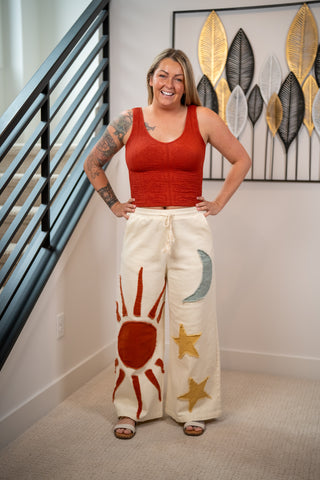 Woman wearing a red top and white pants with sun and star designs indoors.