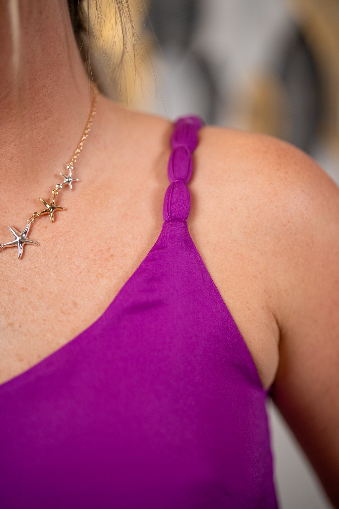 Close-up of a person wearing a purple top and gold necklace with starfish charms.