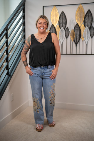 Woman wearing a black top and blue jeans with floral embroidery indoors.