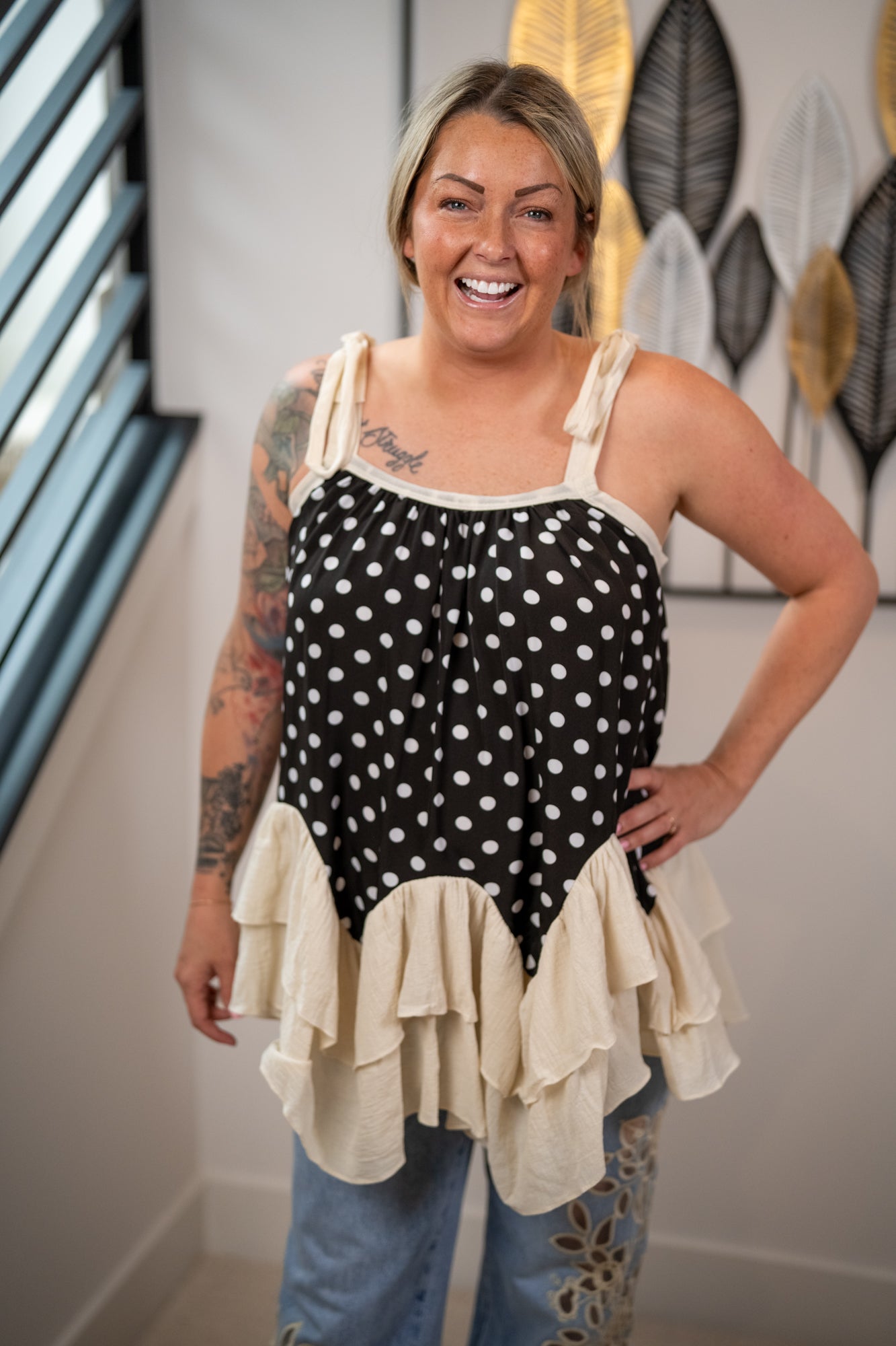 Woman wearing a black polka dot top with ruffled layers in a room with decorative wall art.