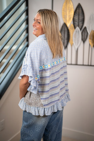 Woman wearing a light blue and gray striped shirt with floral embellishments in a room.