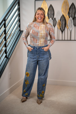 Woman wearing a patterned top and floral jeans in a room with decorative wall art.