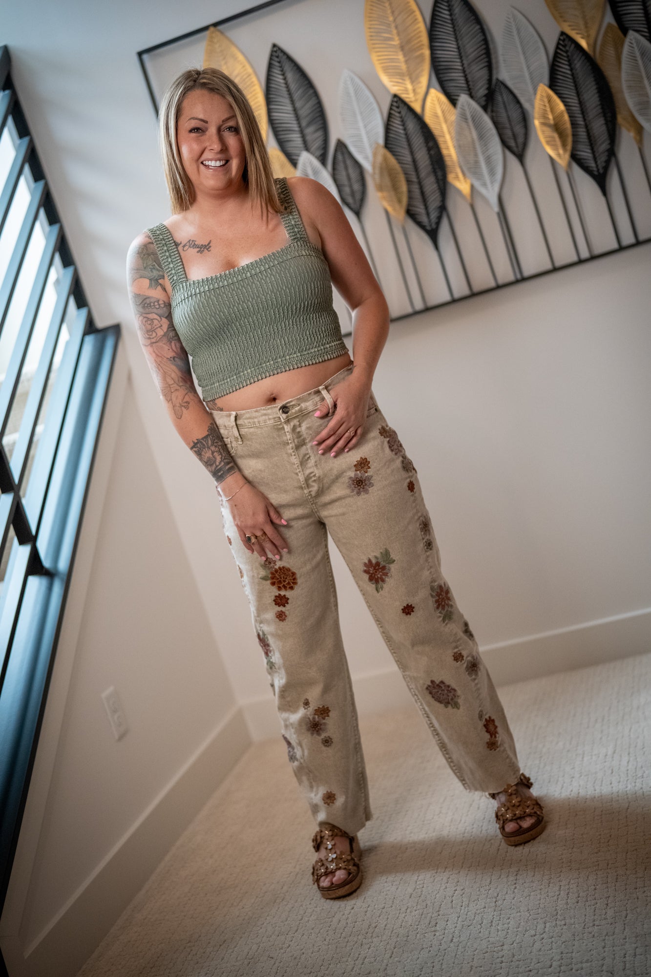Woman wearing a green crop top and beige pants with floral patterns in a room.