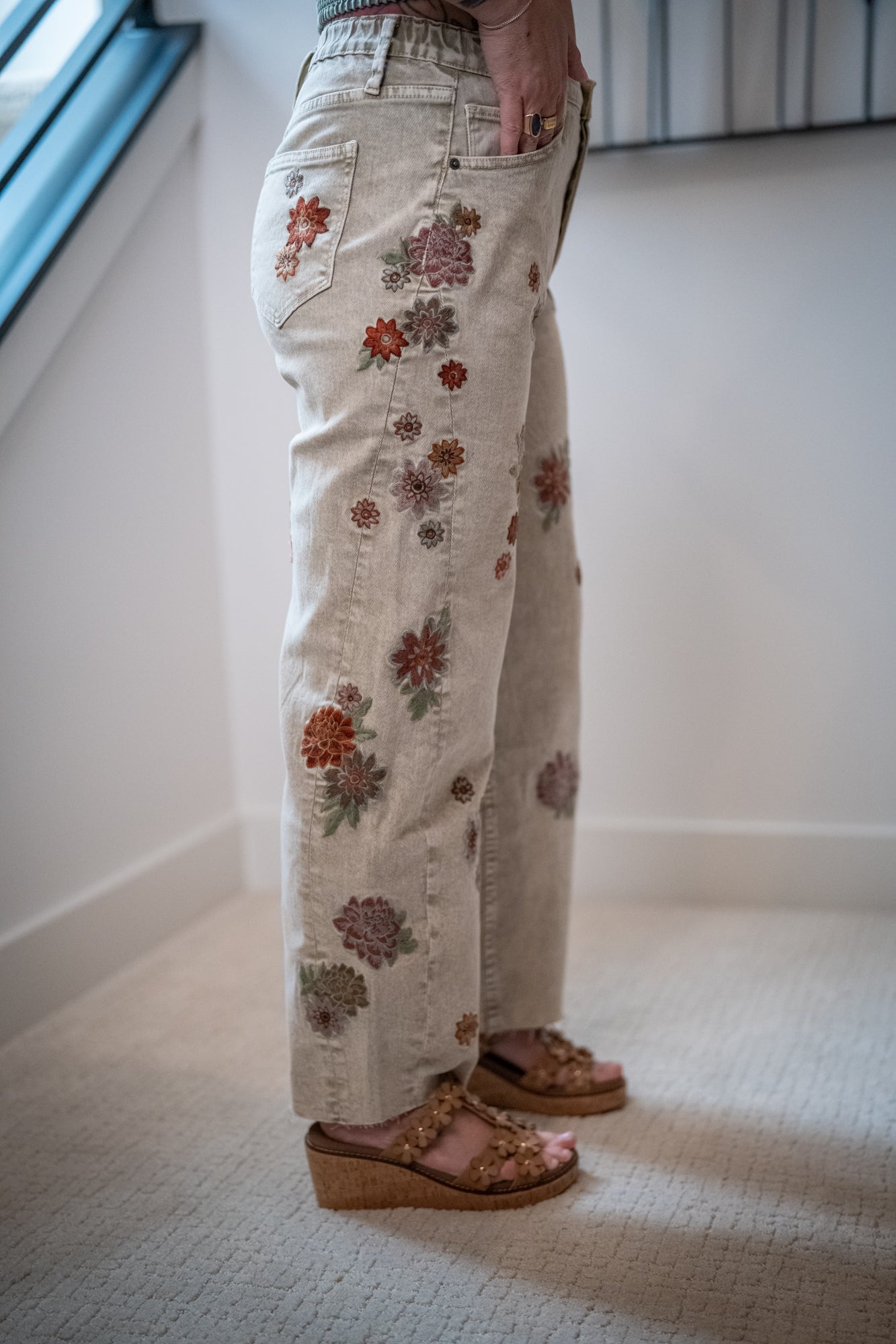 Person wearing floral-patterned pants standing indoors on a carpeted floor.