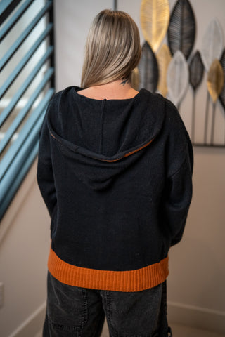 Black knit hoodie with burnt orange hem and hood trim, back view