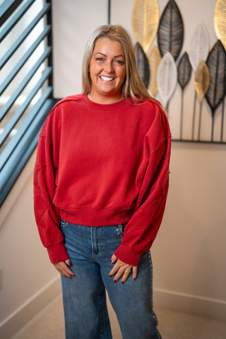 Red crew neck sweatshirt with star patch sleeves, worn with blue jeans