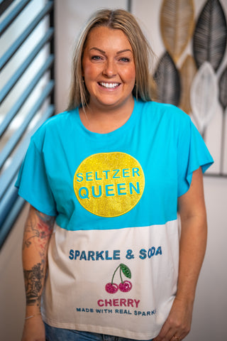 Person wearing a colorful t-shirt with 'Seltzer Queen' text and graphics.