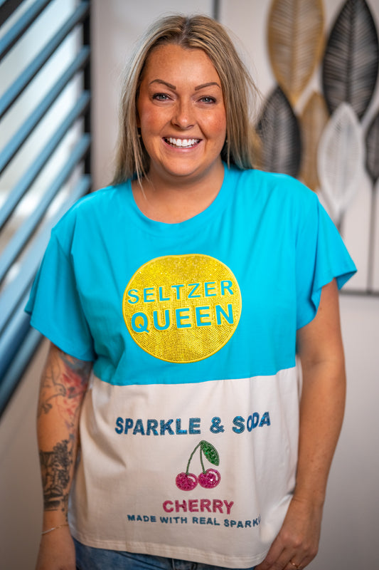 Person wearing a colorful t-shirt with 'Seltzer Queen' text and graphics.