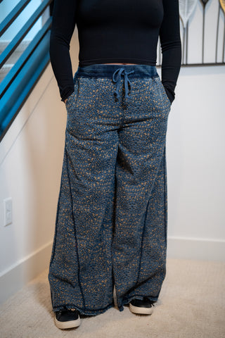 Person wearing blue patterned pants with a black top indoors.