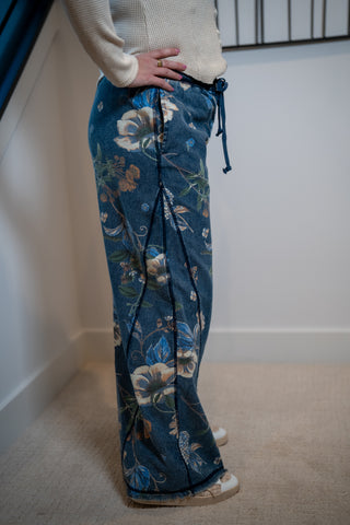 Person wearing blue floral pants standing in a room with white walls and a carpeted floor.