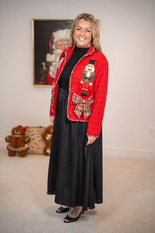 Red quilted jacket with nutcracker appliqué and plaid bow, worn over black dress