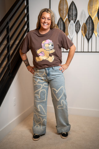 Woman wearing a graphic t-shirt and jeans standing indoors with decorative wall art in the background.